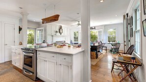 A spacious kitchen with white cabinetry, a large island, and a dining area with a table and chairs. - Pau Hana - Spacious 4-bedroom house in quaint Nantucket with AC (Nantucket)