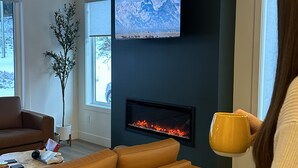 Una sala de estar con chimenea, un televisor montado en la pared y un ventanal grande.