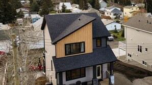 Una casa moderna de dos pisos con techo oscuro, sección frontal de madera y un balcón.