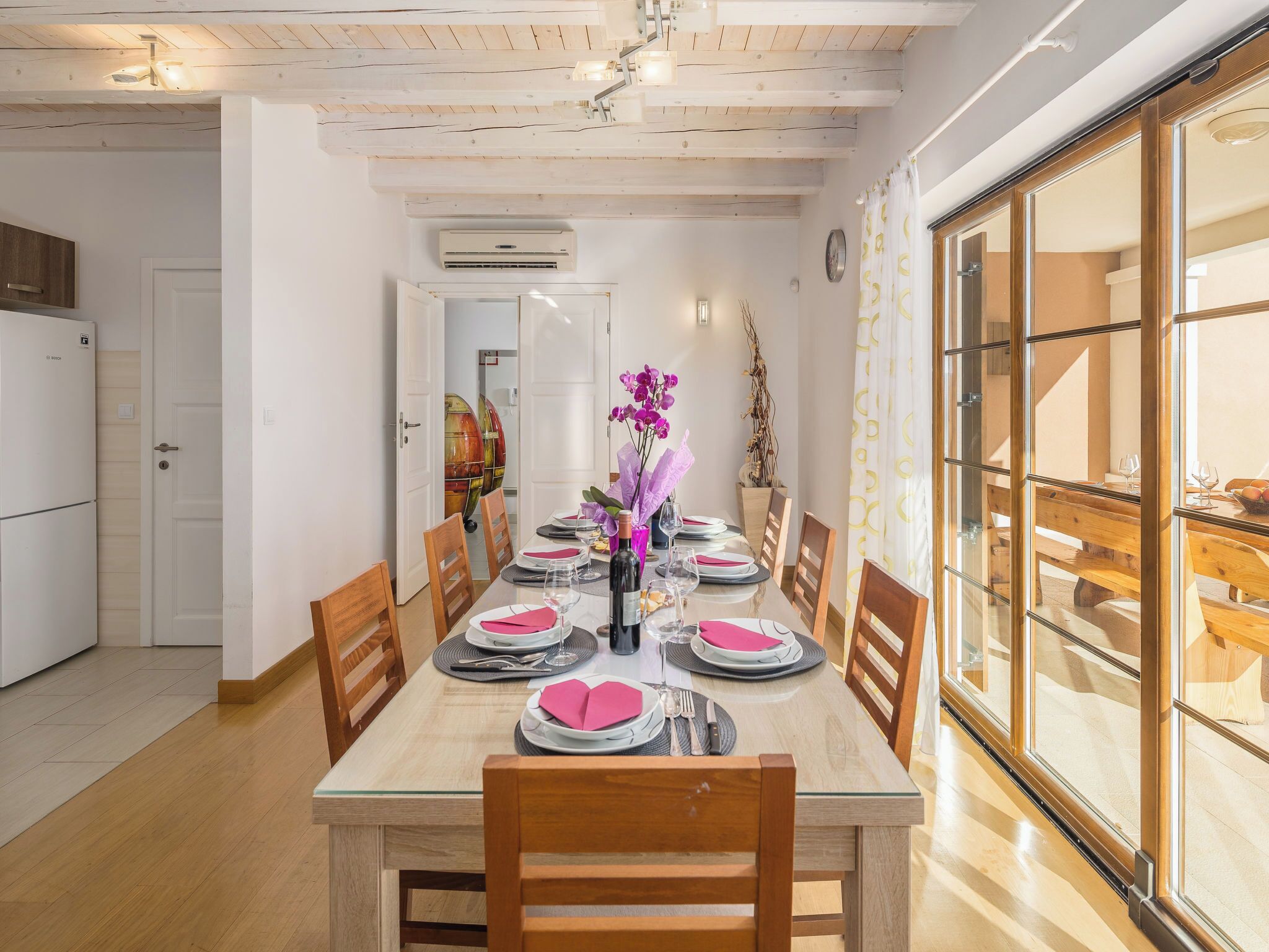Un comedor con una mesa de madera dispuesta para seis personas, rodeada de sillas, y un separador de vidrio en un lateral.