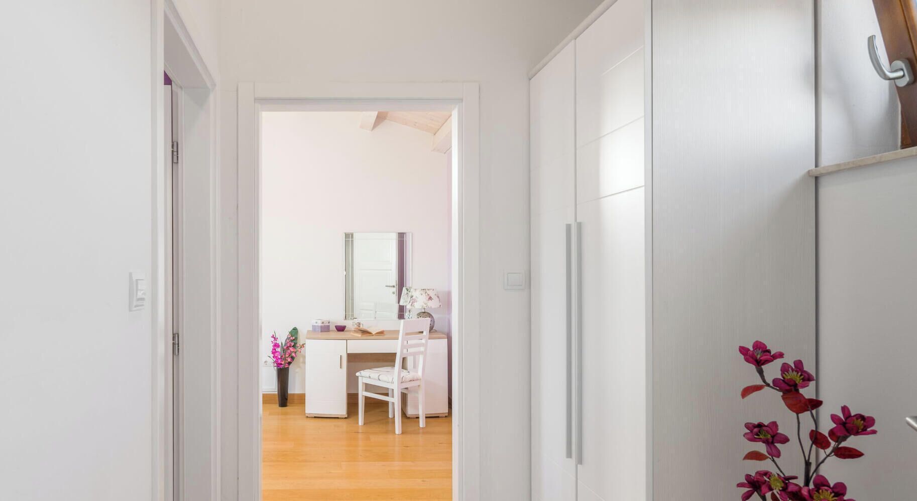 Un couloir menant à une pièce où se trouvent un bureau, une chaise et un miroir.
