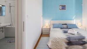 Ein Schlafzimmer mit einem Bett, Nachttischen, einem Wandbild und einem durchgehenden Türspalt sichtbaren Badezimmer.