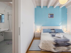 Ein Schlafzimmer mit einem Bett, Nachttischen, einem Wandbild und einem durchgehenden Türspalt sichtbaren Badezimmer.