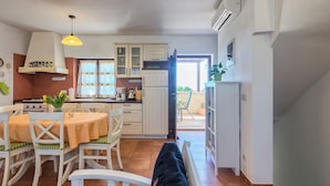Een keuken met witte kastjes, een eettafel met stoelen, een fornuis en een open deur die leidt naar een balkon.