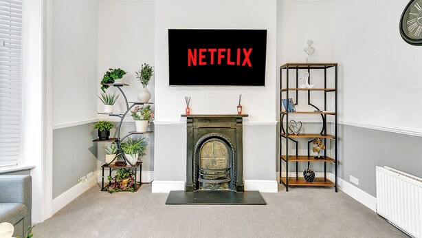 En opholdsstue med pejs, et ophængt fjernsyn der viser "NETFLIX" og en reol.