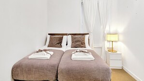 En dobbeltseng med to puder, et natbord med lampe, og et vindue med let gardin.