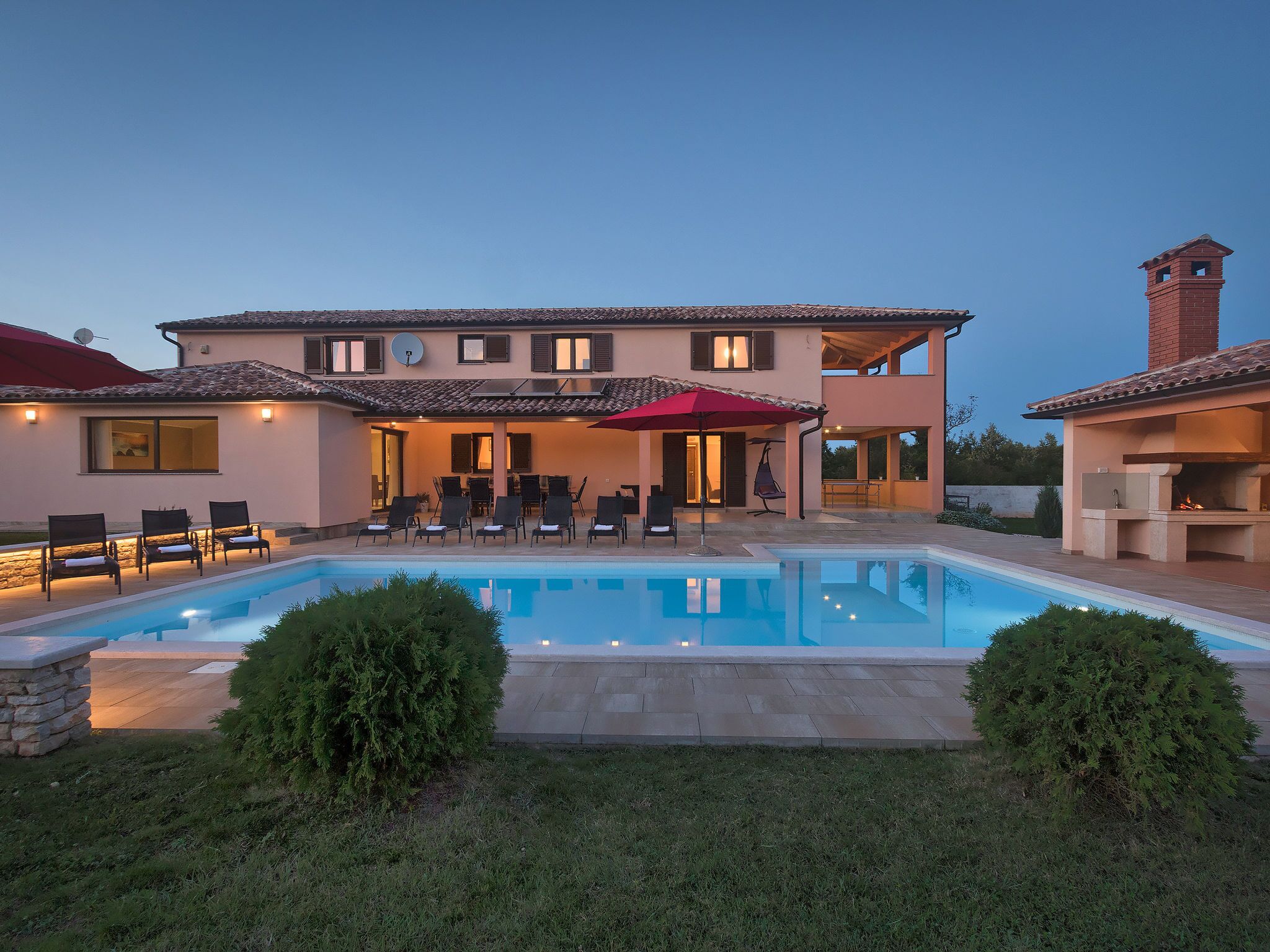 Ein zweigeschossiges Haus mit Swimmingpool, Außenbereich mit Sitzgelegenheiten und Grillplatz.