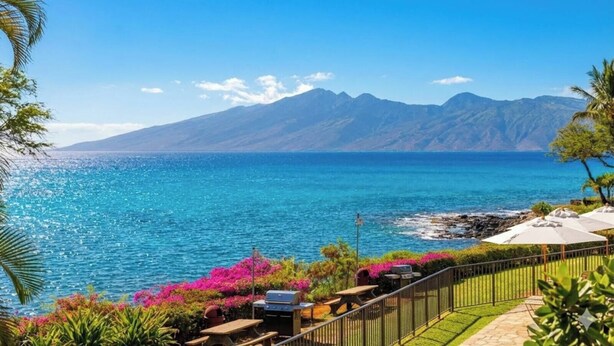 Une vue sur la côte, avec une chaîne de montagnes en arrière-plan, un ciel dégagé et un espace patio aménagé avec des sièges d’extérieur et un barbecue.