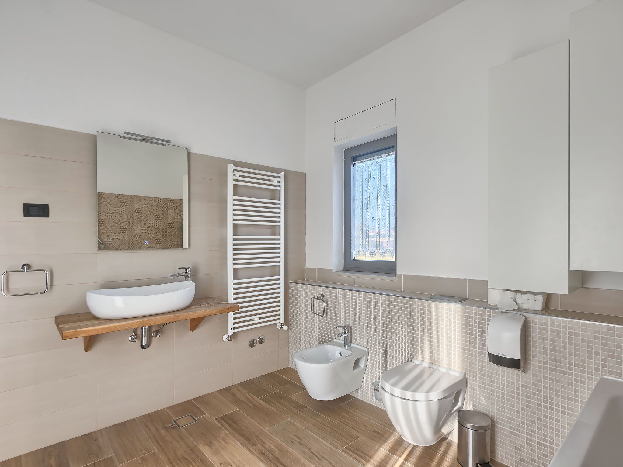 A modern bathroom with a freestanding sink, a towel rack, a toilet, and a window.