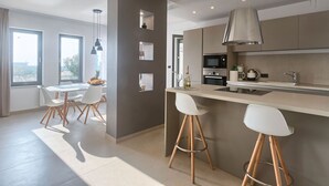 A modern kitchen with a central island, bar stools, a dining area with a table and chairs, and a view through the windows. - Villa Volimten by Interhome (Pula/Vodnjan)