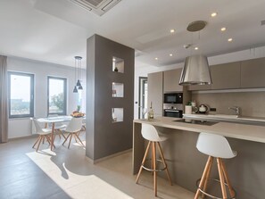 A modern kitchen with a central island, bar stools, a dining area with a table and chairs, and a view through the windows. - Villa Volimten by Interhome (Pula/Vodnjan)