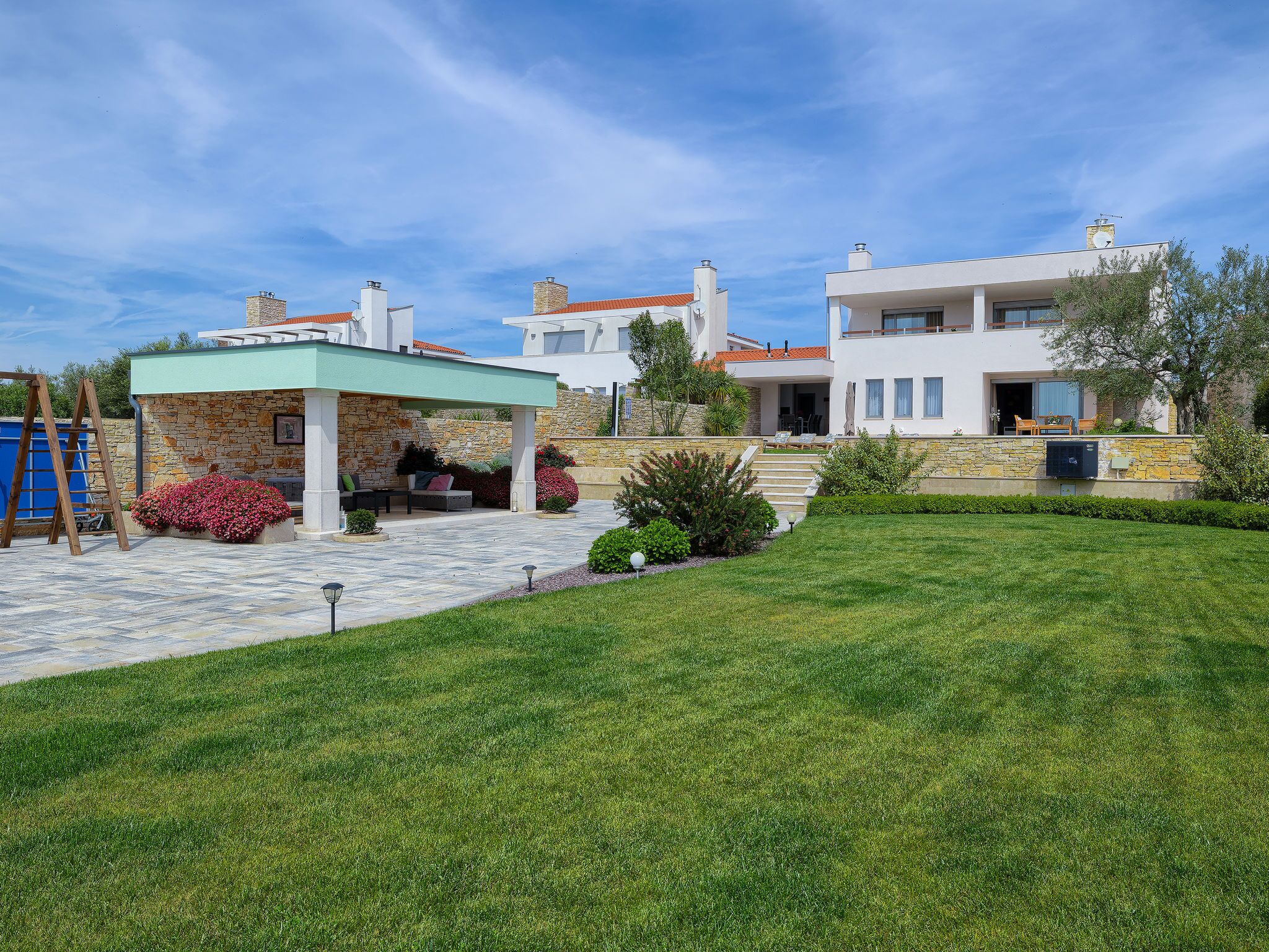 Eine moderne Villa mit Steinverkleidung, einer überdachten Terrasse und einem gepflegten Rasen.