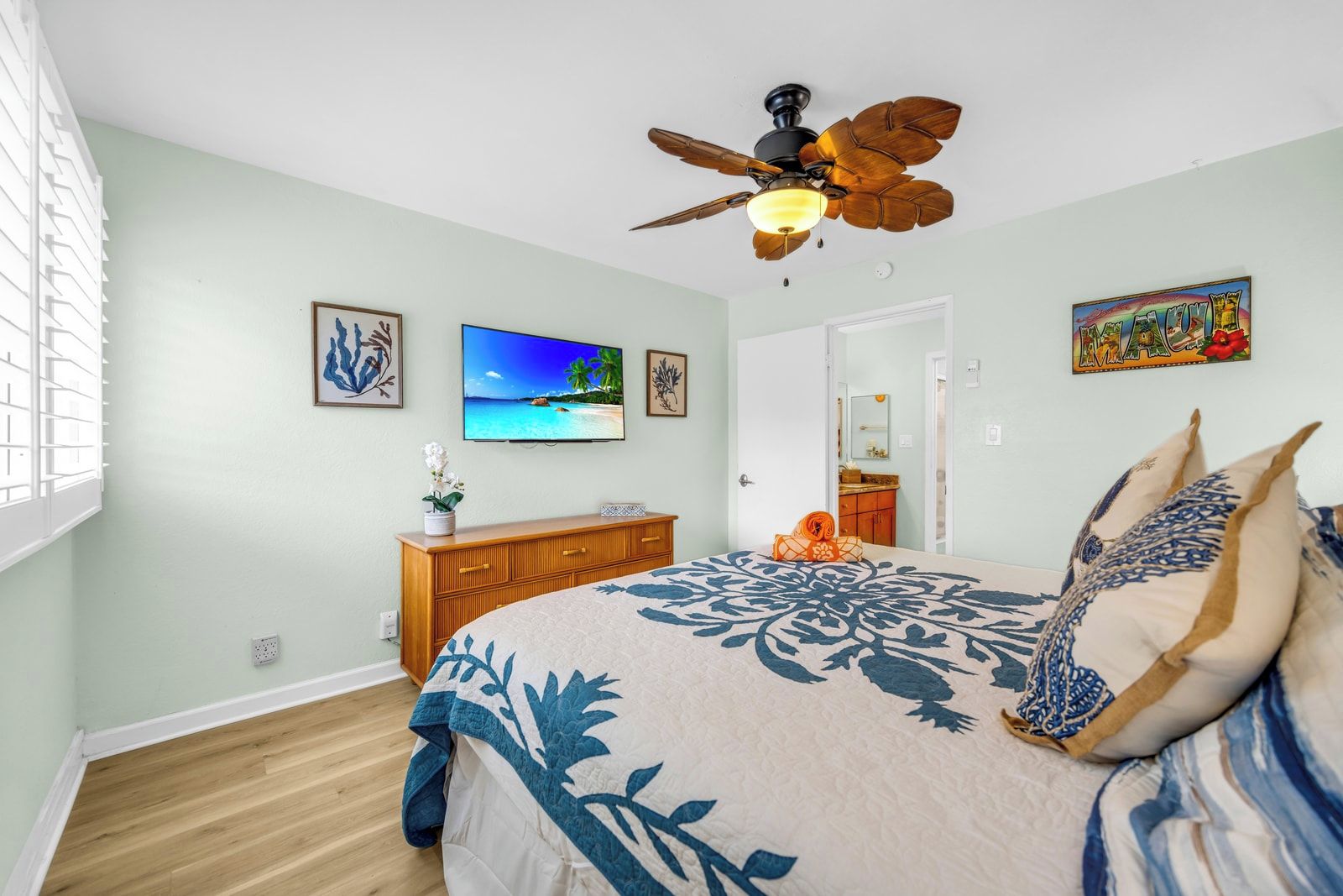 A bedroom with a bed, a ceiling fan, a TV, and a door leading to a bathroom.