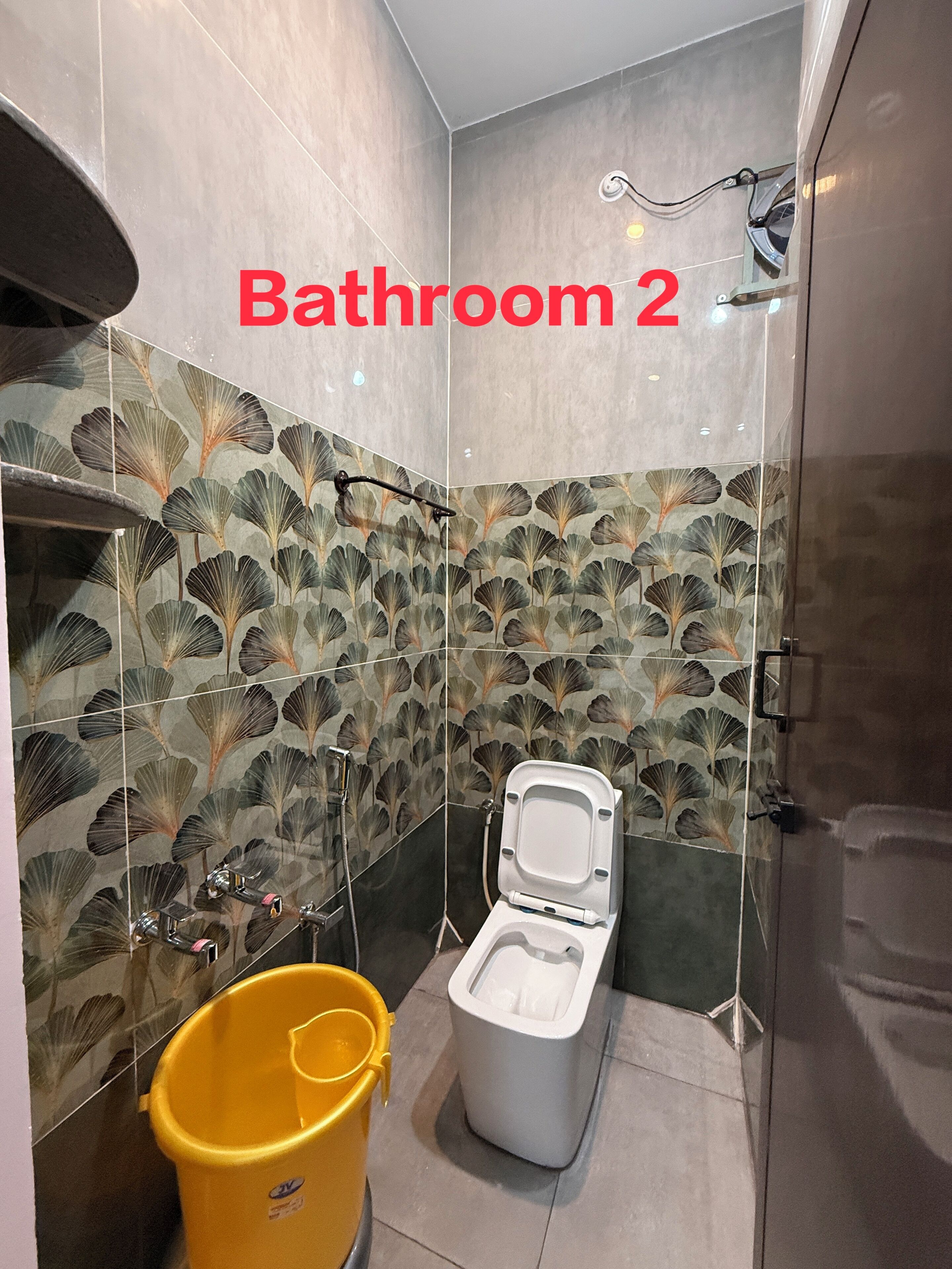 Un bagno con il water, una doccia e un secchio giallo.