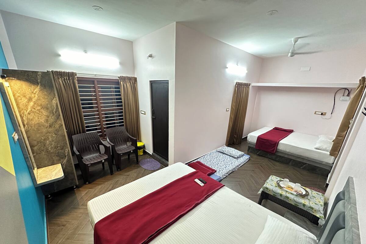 A hotel room with two beds, a small table, a chair, and a window with curtains.