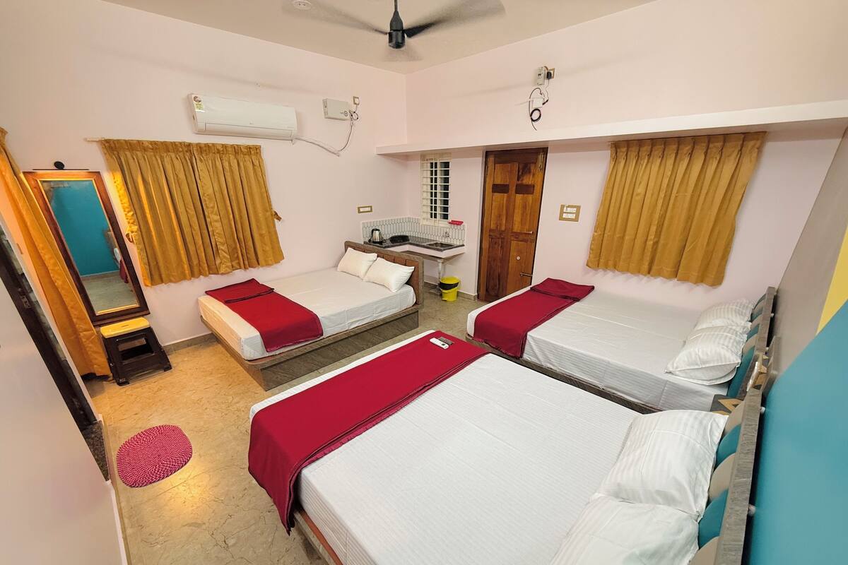 A hotel room with three single beds, a small bathroom, and a ceiling fan.