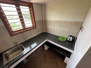 A small kitchen with a window, a sink, a green plate, and a kettle. - OM LINGESWARAN Home Stay Tiruvannamalai (Tiruvannamalai)