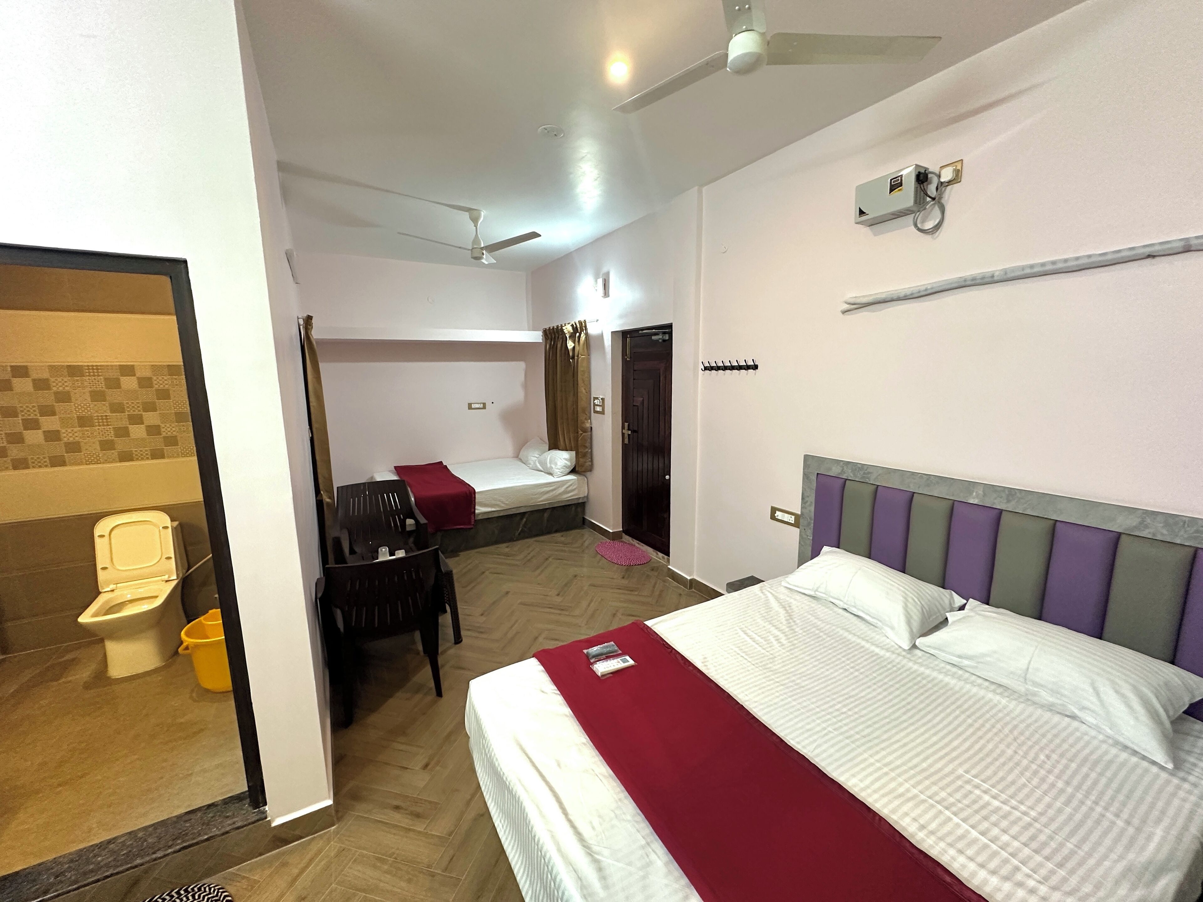 A hotel room with a bed, a desk, a chair, a bathroom with a toilet, and a ceiling fan.