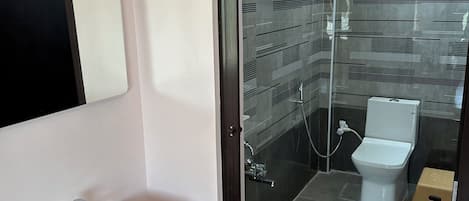 A bathroom with a white sink, a mirror, a yellow bucket, a toilet, and a shower area.