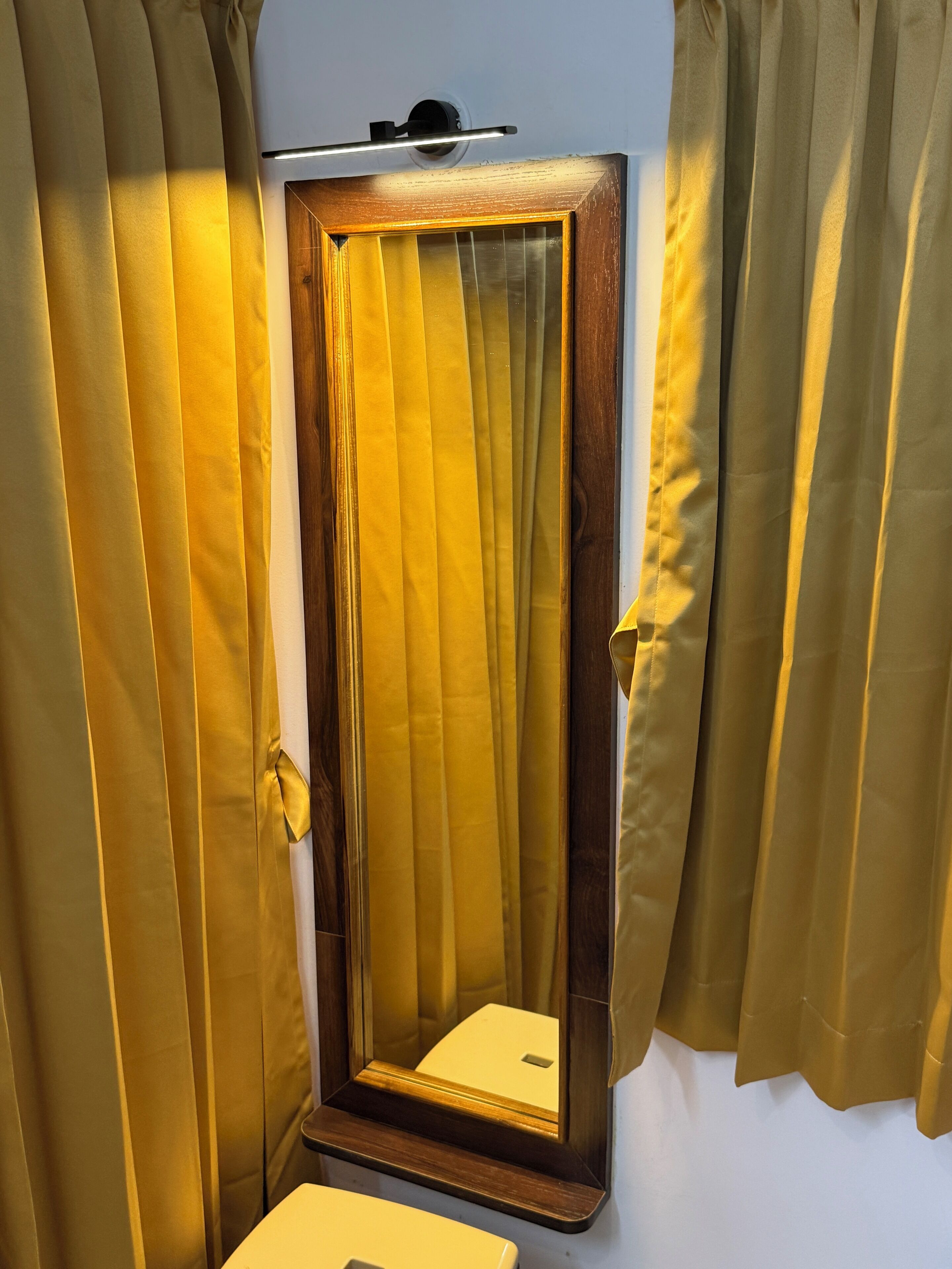 A mirror with a wooden frame, flanked by curtains, in a room with a white wall and a small table.