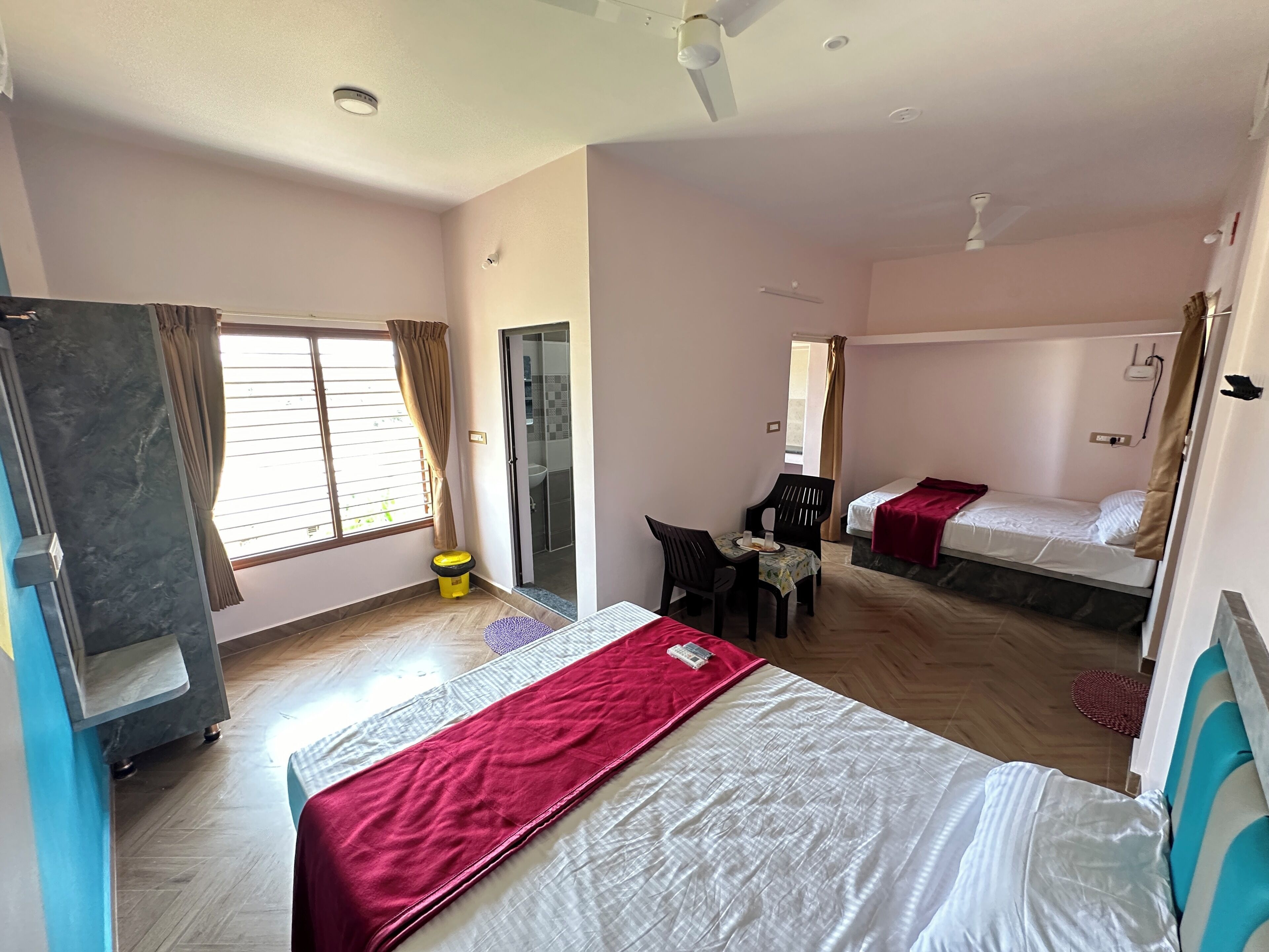 Habitación de hotel con cama, escritorio, silla, ventana con cortinas, baño y ventilador de techo.