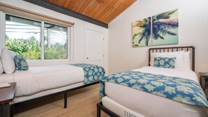 Una camera da letto con due letti, una finestra, travi a vista al soffitto e un'opera d'arte appesa al muro.