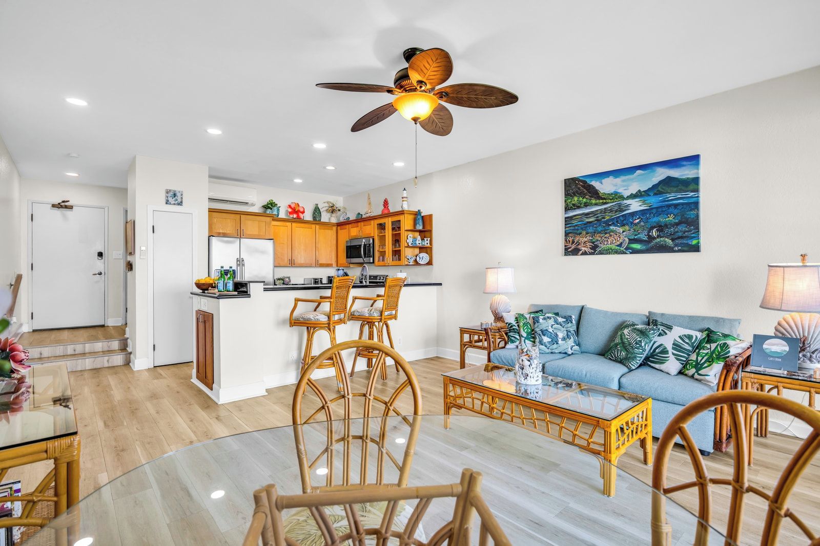 Une cuisine moderne avec des meubles en bois, un coin repas avec des chaises en osier, un canapé bleu et un ventilateur de plafond.