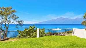 Un'area verde con una recinzione in metallo, un muro bianco e vista sull'oceano e sulle montagne.
