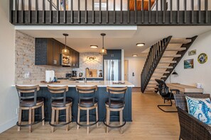 A modern kitchen with a central island, bar stools, and a staircase leading to an upper level. - Napili Point | Oceanfront 4 BR, Sleeps 12 | Car Incl. w/ 6+ Nights | NAP ML-3604 by KBM (Lahaina)