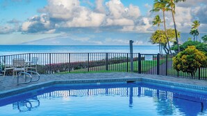 A swimming pool with a view of the ocean, a fenced area with chairs, and palm trees. - Napili Point | Oceanfront 4 BR, Sleeps 12 | Car Incl. w/ 6+ Nights | NAP ML-3604 by KBM (Lahaina)