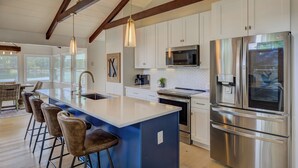 A modern kitchen with a large island, stainless steel appliances, and a farmhouse-style ceiling.