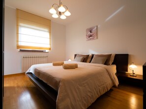 Ein Schlafzimmer mit einem großen Bett, einem Heizkörper, einem Fenster mit Jalousien, einem Wandbild und einem Nachttisch mit Lampe.