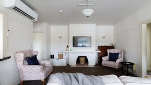 Een woonkamer met een open haard, twee gestreepte fauteuils, een bank en een televisie boven de open haard.
