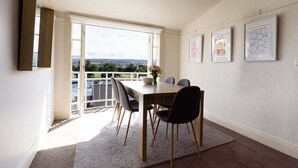 Een eethoek met een tafel en stoelen, een uitzicht door een groot raam, en beelden aan de muur.