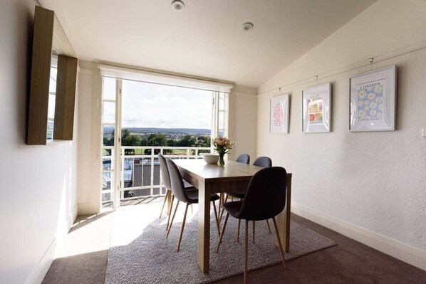 A dining area with a table and chairs, a view through a large window, and framed pictures on the wall. - Tennis or Town - Parking and Wifi (Launceston)