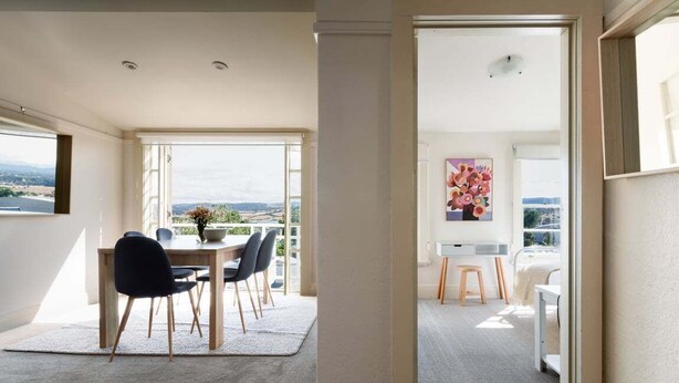 Een modern interieur met een eethoek, een groot raam met uitzicht en een gang naar een slaapkamer.