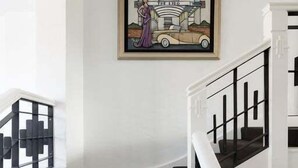 Een trap met zwarte leuningen en een donker tapijt, die uitkomt op een plateau met een kunstwerk in een lijst waarop een oldtimer en een vrouw staan afgebeeld.