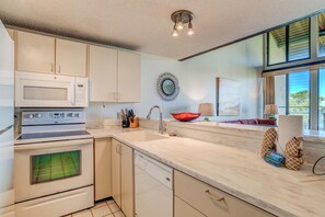 Une cuisine moderne avec des meubles blancs, un four à micro-ondes, une cuisinière et un lave-vaisselle. Une fenêtre offre une vue sur la verdure environnante.
