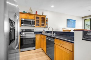 A modern kitchen with stainless steel appliances, wooden cabinets, and a black countertop. - Napili Point | Oceanfront 6 BR, Sleeps 18 | Car Incl. w/ 6+ Nights | NAP ML-3610 by KBM (Lahaina)
