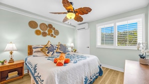 Ein Schlafzimmer mit Bett, Deckenventilator, Fenster mit Jalousien und Wanddekoration.