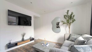 Un salon moderne avec un téléviseur à écran plat, un canapé, une table basse et une plante décorative.