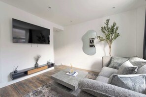 A modern living room with a flat-screen TV, a sofa, a coffee table, and a decorative plant.