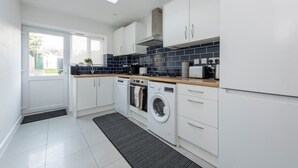 Une cuisine moderne avec des meubles blancs, un lave-linge encastré et une lucarne.