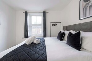 Une chambre d’hôtel avec un lit, une fenêtre avec des rideaux, une tête de lit et un porte-manteau fixé au mur.