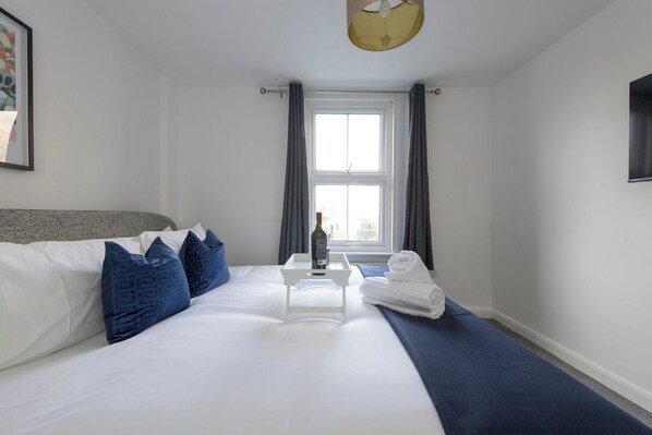 A hotel room with a large bed, a bedside table with a bottle, a folded towel, and a window with curtains.
