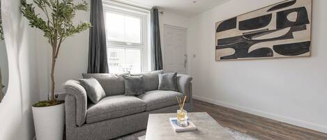 A living room with a grey sofa, a coffee table, a potted plant, and a large abstract painting on the wall.