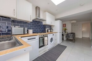 A modern kitchen with white cabinets, a microwave, a stove, and a washing machine.
