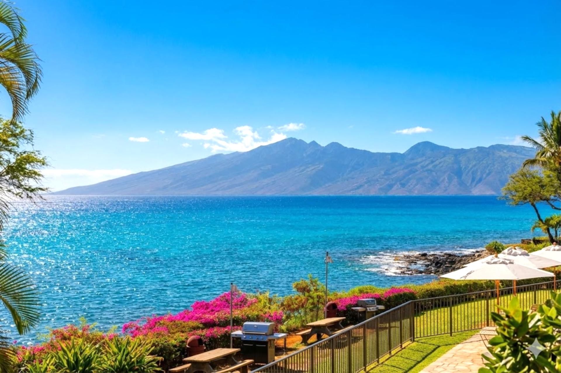 A coastal view with a mountain range, a clear sky, and a patio area with outdoor seating and a barbecue grill.