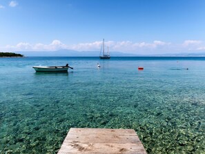 A wooden dock extending into clear, shallow water with a boat and a sailboat anchored in the distance. - Apartment Janko by Interhome (Krk/Njivice)