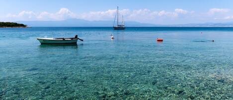 Un muelle de madera se extiende sobre aguas claras y poco profundas, con un bote y un velero anclados en la distancia.